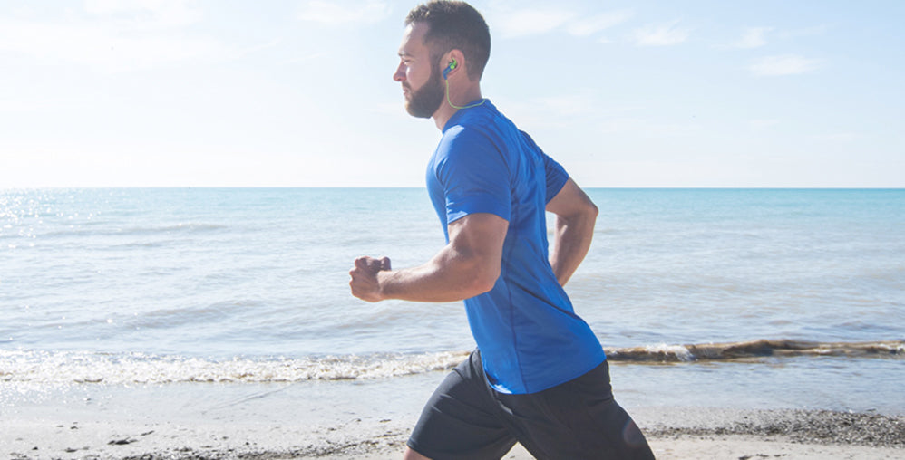 Man running at the beach wearing Koss Headphones