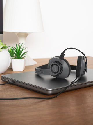 KPH30 Wireless in grey on a desk plugged into a laptop headphone jack with the Koss KUSB-50 USB-C to 3.5mm Analog Audio Pass Through cord.