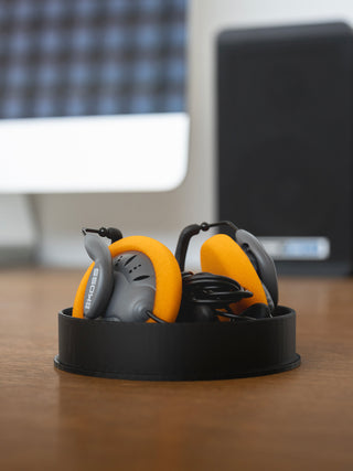 Orange and gray headphones in a black holder on a desk with a blurred office background