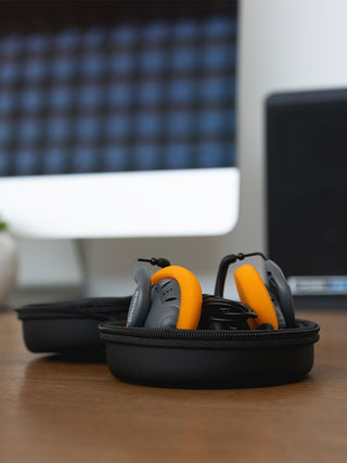 Orange and gray ear defenders in a black case on a desk with a blurred office background