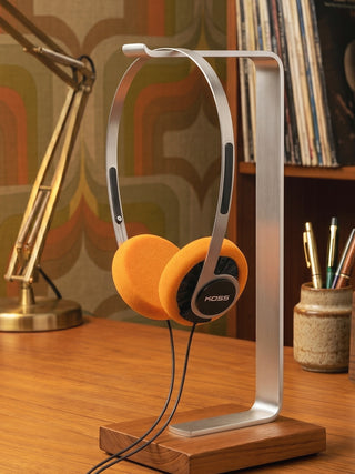 Orange headphones on a stand with a lamp and books in the background