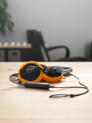 Orange and black headphones on a wooden table with a blurred office background