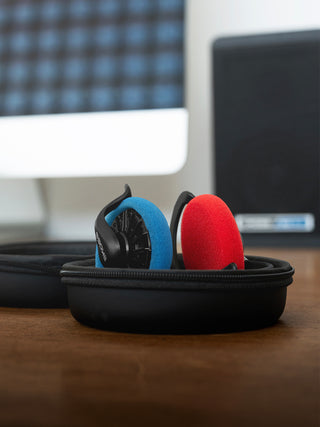 Colorful ear protection devices in a black case on a desk with computer monitors in the background.