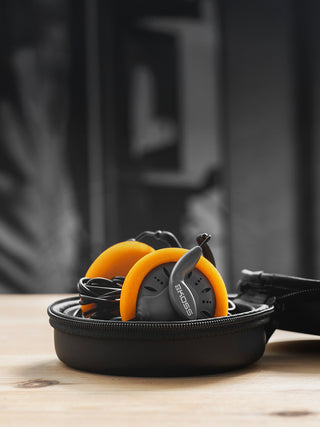 Orange earbuds in a black case on a wooden surface with a blurred background