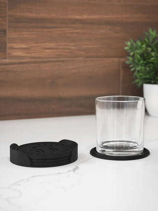 Black coasters with a glass on a white surface against a wooden wall.
