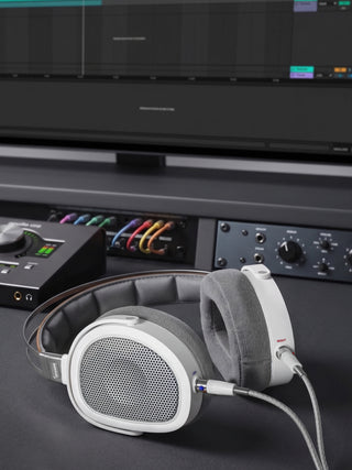 Pair of headphones on a dark surface with audio equipment in the background