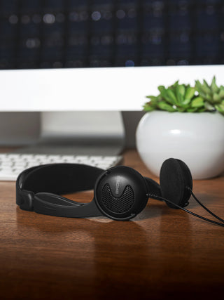 Black headphones on a wooden desk with a computer monitor and plant in the background