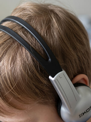 Close-up of a child wearing black and white headphones with 'Koss' branding.