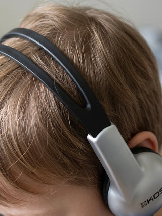 Close-up of a child wearing over-ear headphones with a black and silver headband and ear cup, shown from the side.